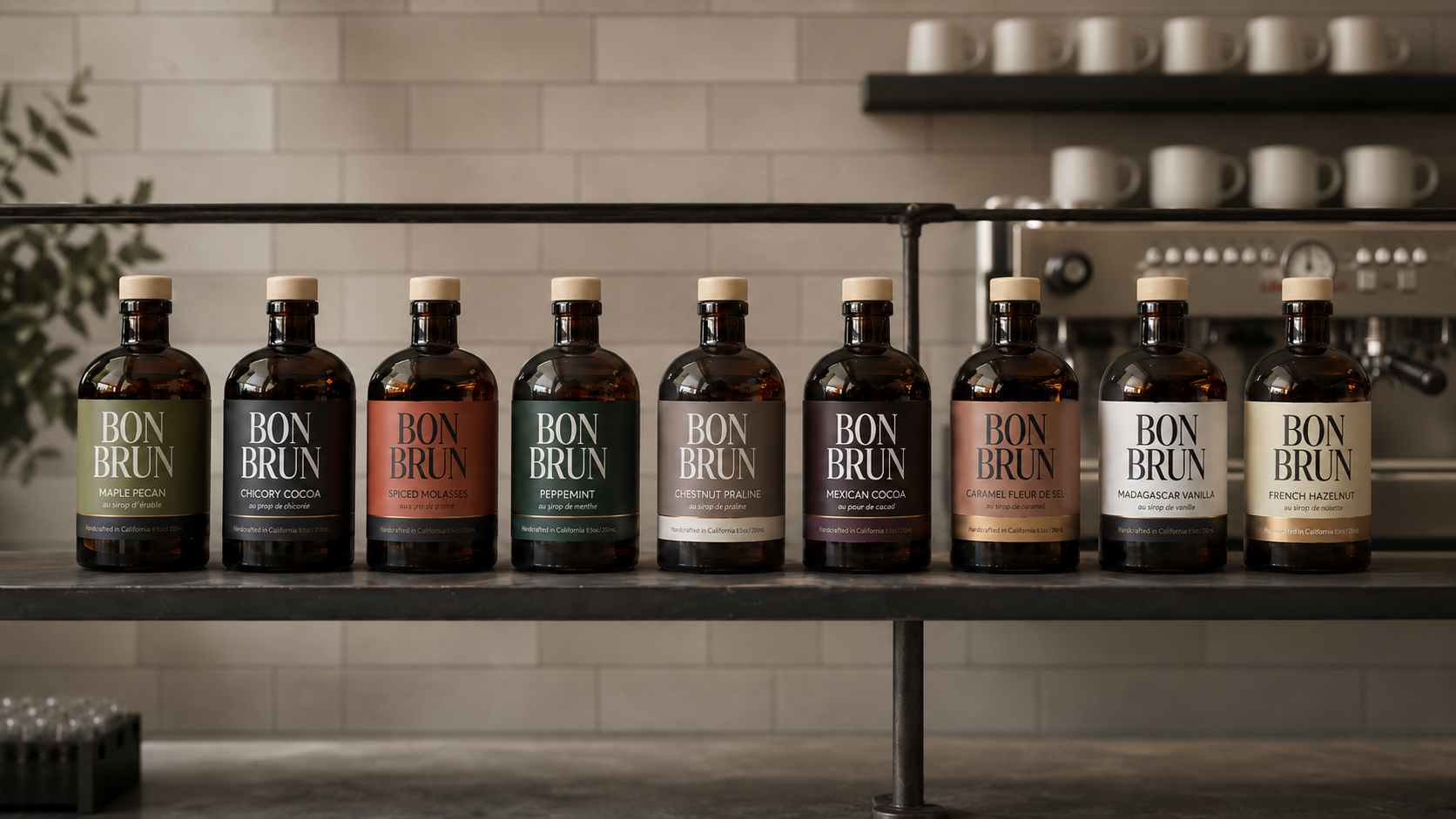 Nine bottles of Bon Brun coffee syrups lined up on a shelf in a kitchen setting, showing a range of roasting profiles from light to dark.